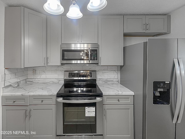 kitchen with light stone countertops, backsplash, appliances with stainless steel finishes, and gray cabinets