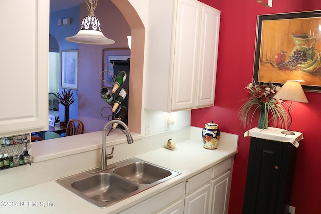 kitchen with decorative light fixtures, sink, and white cabinets