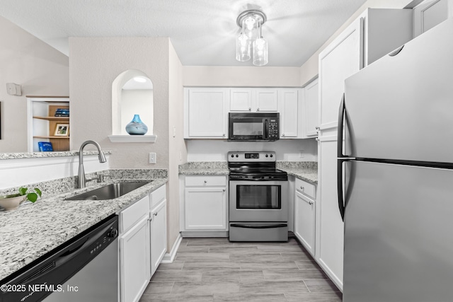 kitchen featuring sink, appliances with stainless steel finishes, white cabinetry, light stone countertops, and a textured ceiling