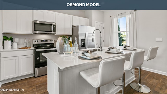 kitchen with white cabinets, dark hardwood / wood-style floors, a kitchen island with sink, and appliances with stainless steel finishes