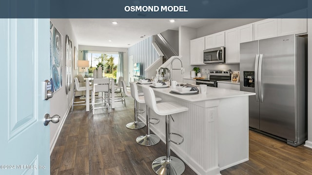 kitchen with white cabinetry, a kitchen island with sink, appliances with stainless steel finishes, and dark wood-type flooring