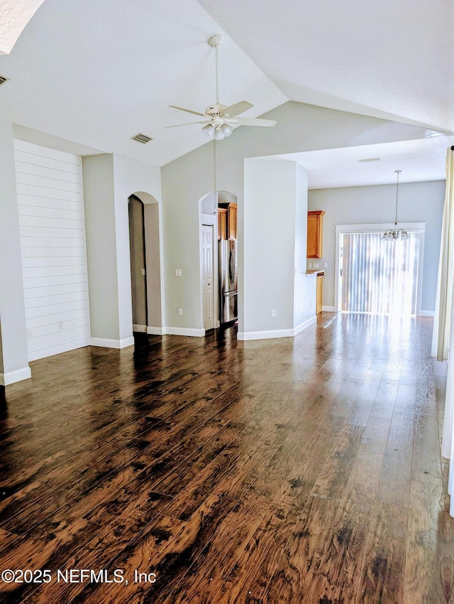 unfurnished living room with dark hardwood / wood-style flooring, ceiling fan with notable chandelier, and vaulted ceiling