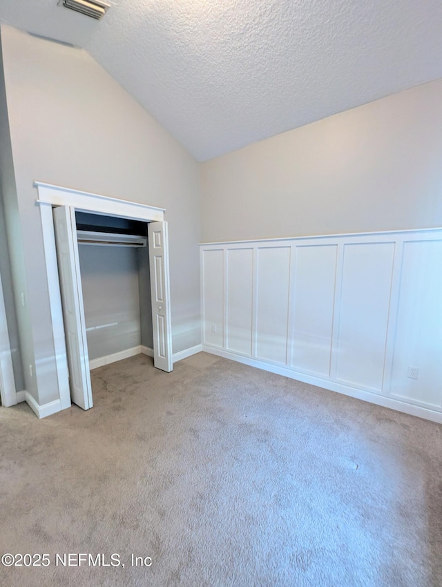 unfurnished bedroom with a closet, light colored carpet, vaulted ceiling, and a textured ceiling