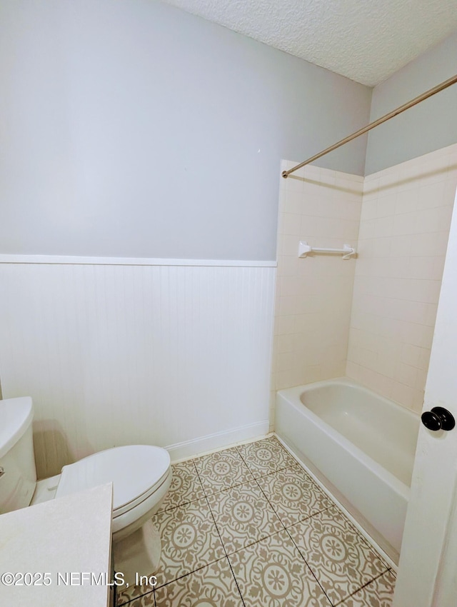 bathroom featuring tiled shower / bath, tile patterned floors, a textured ceiling, and toilet