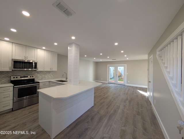 kitchen with sink, hardwood / wood-style floors, stainless steel appliances, white cabinets, and kitchen peninsula