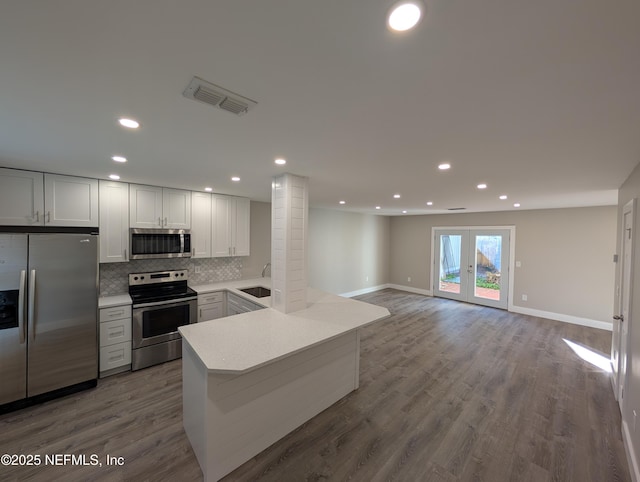 kitchen with hardwood / wood-style floors, tasteful backsplash, sink, kitchen peninsula, and stainless steel appliances