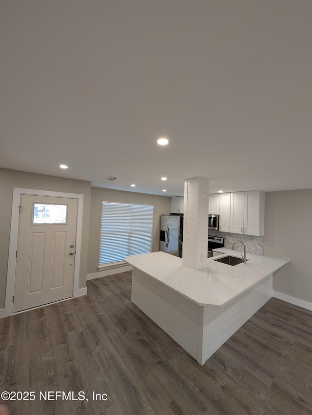 kitchen with sink, white cabinetry, appliances with stainless steel finishes, kitchen peninsula, and backsplash