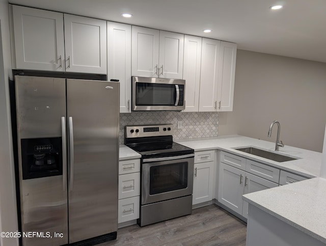 kitchen with appliances with stainless steel finishes, sink, white cabinets, and light wood-type flooring