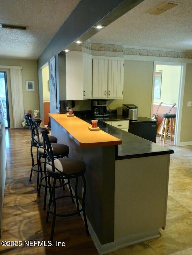 kitchen featuring a textured ceiling, a breakfast bar, white cabinetry, and kitchen peninsula