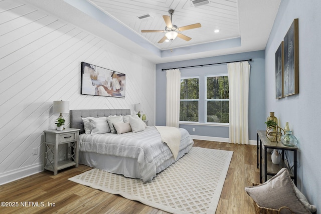 bedroom with ceiling fan, wood-type flooring, and a tray ceiling