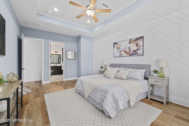 bedroom with a tray ceiling, light hardwood / wood-style floors, ceiling fan, and ensuite bathroom