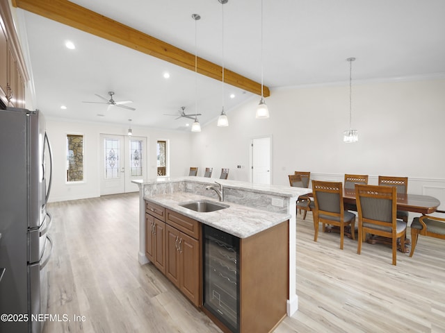 kitchen featuring pendant lighting, sink, stainless steel refrigerator, wine cooler, and an island with sink