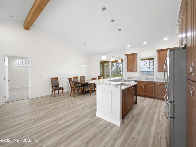 kitchen featuring pendant lighting, crown molding, stainless steel fridge, light stone counters, and a center island with sink