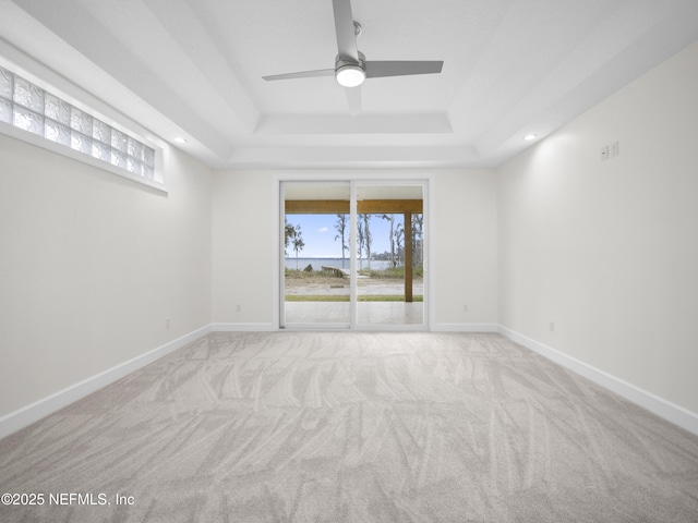 empty room with a raised ceiling, light colored carpet, and ceiling fan