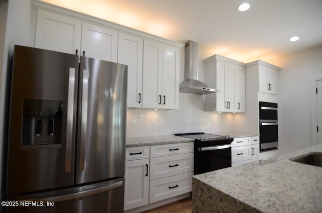 kitchen featuring stainless steel refrigerator with ice dispenser, black electric range oven, wall chimney exhaust hood, white cabinets, and light stone countertops