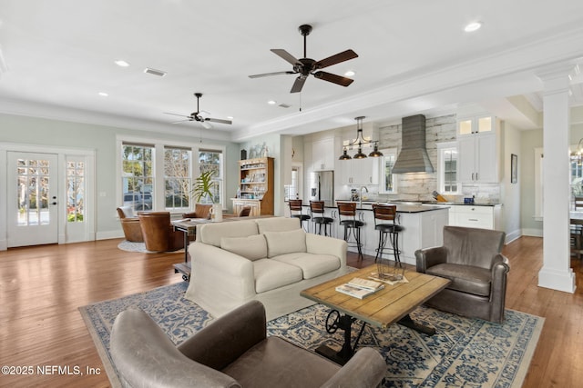 living room with decorative columns, ornamental molding, ceiling fan, and light wood-type flooring