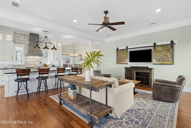 living room featuring dark wood-type flooring, ornamental molding, and ceiling fan with notable chandelier