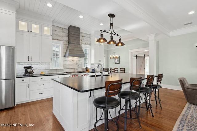 kitchen with sink, custom exhaust hood, a center island with sink, stainless steel fridge, and a barn door