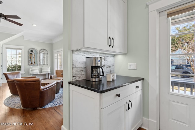 kitchen featuring hardwood / wood-style flooring, crown molding, ceiling fan, white cabinetry, and backsplash