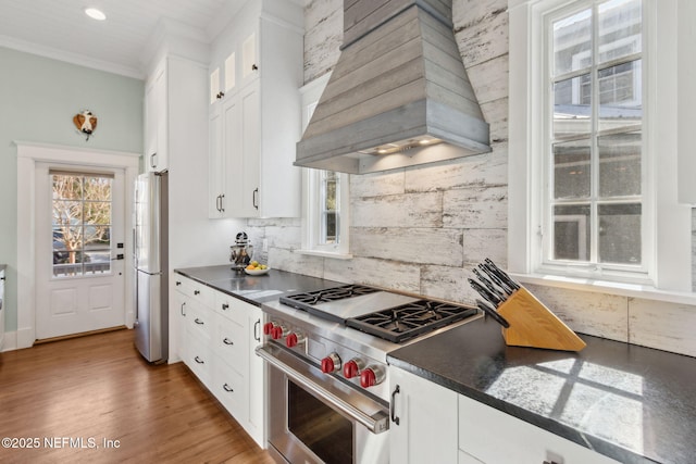 kitchen featuring backsplash, white cabinets, high end range, fridge, and custom range hood