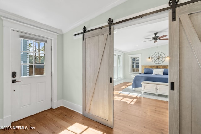 doorway to outside with crown molding, a barn door, lofted ceiling, and light hardwood / wood-style flooring