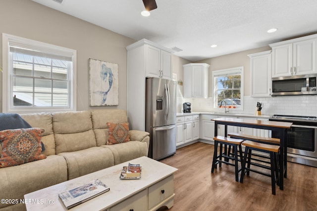 kitchen featuring appliances with stainless steel finishes, sink, white cabinets, decorative backsplash, and light hardwood / wood-style flooring