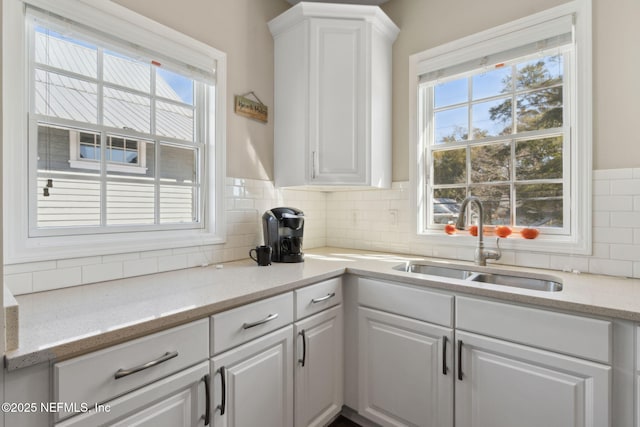 kitchen featuring light stone counters, sink, decorative backsplash, and white cabinets