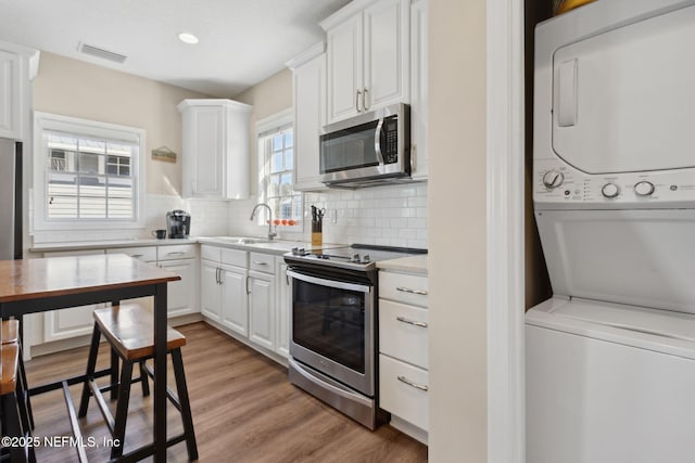 kitchen with sink, appliances with stainless steel finishes, white cabinetry, stacked washer / drying machine, and decorative backsplash