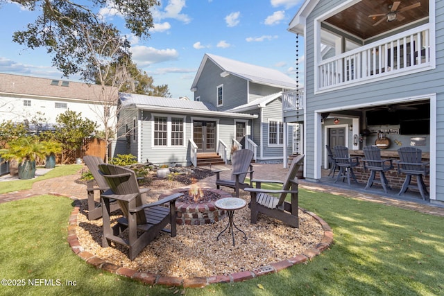 rear view of house with a balcony, a fire pit, a yard, ceiling fan, and a patio area