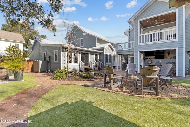 rear view of property with ceiling fan, a balcony, a fire pit, and a lawn