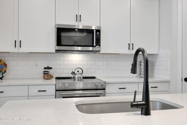 kitchen featuring appliances with stainless steel finishes, white cabinets, a sink, and decorative backsplash