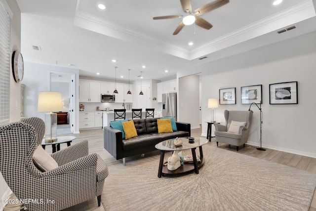 living room with ornamental molding, light wood-type flooring, a raised ceiling, and visible vents