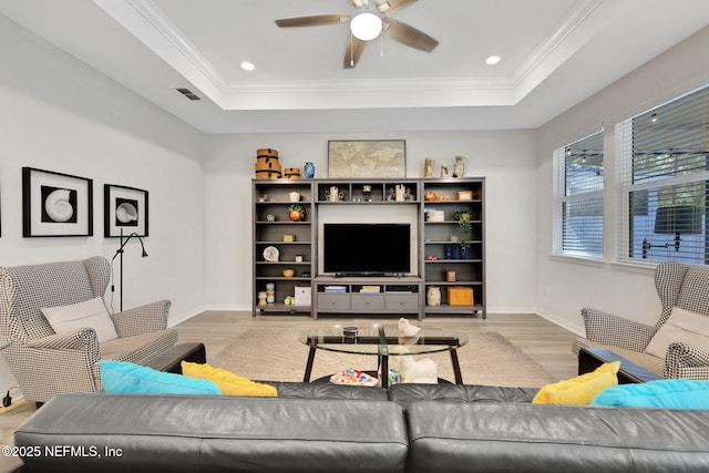 living room with wood finished floors, a raised ceiling, and crown molding