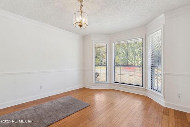 spare room with a notable chandelier, hardwood / wood-style flooring, ornamental molding, and a textured ceiling