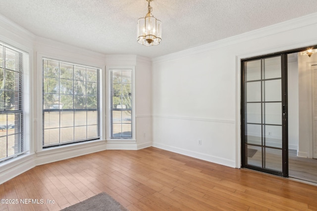 empty room featuring crown molding, a chandelier, a textured ceiling, and light hardwood / wood-style floors