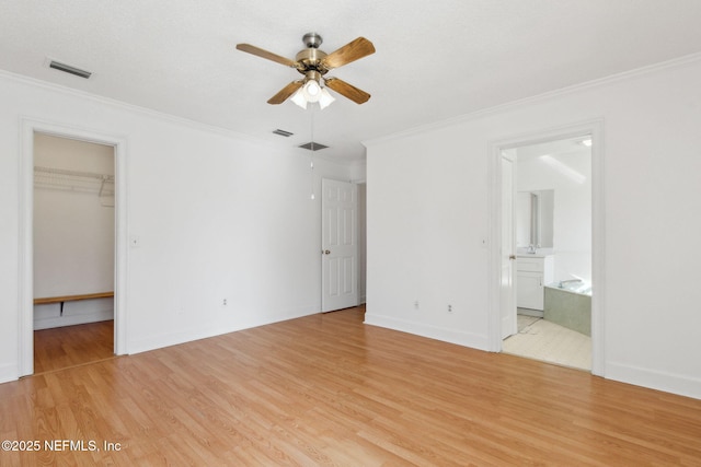 unfurnished bedroom with ornamental molding, a walk in closet, ceiling fan, light hardwood / wood-style floors, and ensuite bath