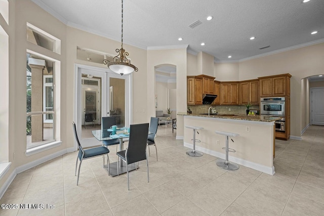 kitchen with decorative light fixtures, light stone counters, crown molding, and a breakfast bar area