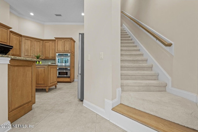 kitchen with light stone countertops, a textured ceiling, stainless steel appliances, light tile patterned floors, and crown molding