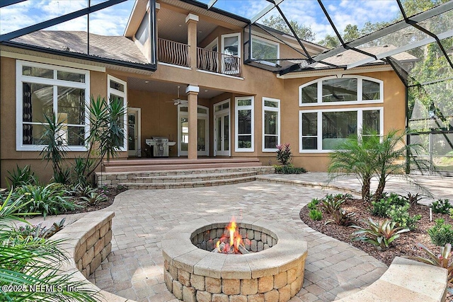 back of property with a lanai, a fire pit, a patio, ceiling fan, and a balcony