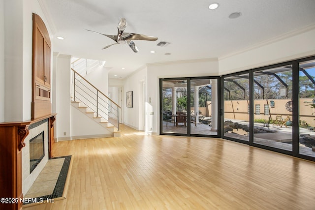 unfurnished living room with a tiled fireplace, ornamental molding, ceiling fan, and light hardwood / wood-style flooring