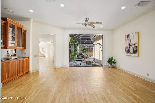 unfurnished room featuring ceiling fan, bar, ornamental molding, and light hardwood / wood-style flooring