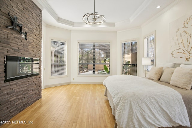 bedroom with a raised ceiling, crown molding, a fireplace, and light hardwood / wood-style floors