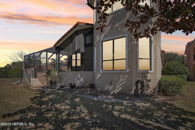 property exterior at dusk featuring a lawn and glass enclosure