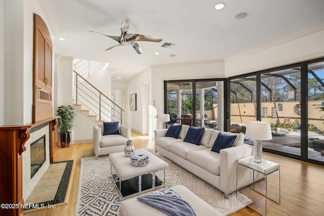 living room featuring a tiled fireplace, crown molding, light hardwood / wood-style floors, and ceiling fan