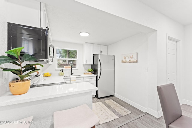 kitchen with sink, white cabinets, stove, light hardwood / wood-style floors, and stainless steel refrigerator