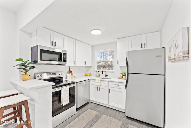 kitchen with sink, white cabinets, light hardwood / wood-style flooring, and stainless steel appliances