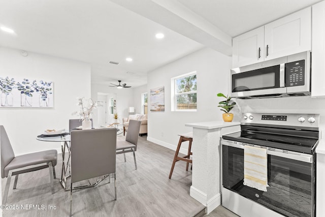 kitchen with appliances with stainless steel finishes, white cabinetry, kitchen peninsula, ceiling fan, and light hardwood / wood-style flooring