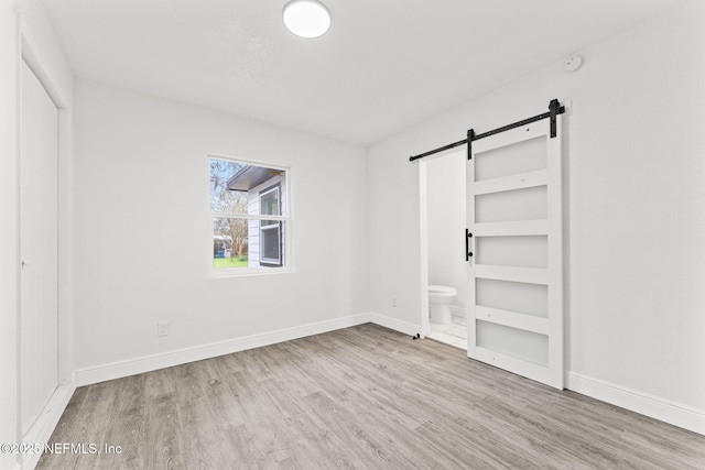 unfurnished bedroom featuring light hardwood / wood-style flooring, ensuite bathroom, and a barn door