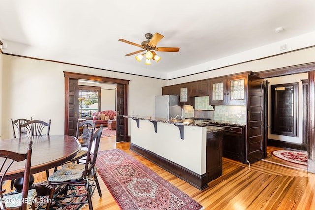 kitchen featuring a kitchen bar, stainless steel fridge, dark brown cabinets, and light wood-type flooring