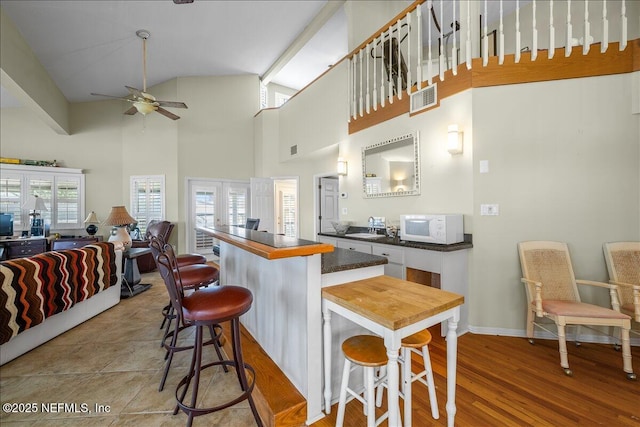 kitchen featuring sink, light hardwood / wood-style flooring, ceiling fan, a kitchen breakfast bar, and a high ceiling